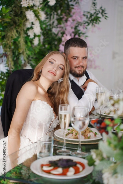 Fototapeta The bride and groom at the newlyweds' table, decorated with many flowers. 