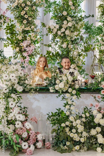 Fototapeta The bride and groom at the newlyweds' table, decorated with many flowers. 