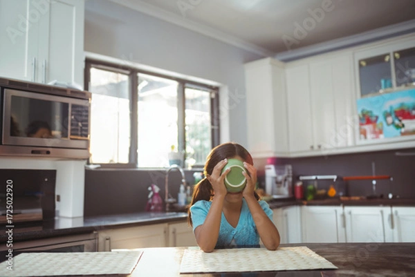 Fototapeta Green mug steaming on wooden table near window with potted plant, microwave on dark countertop