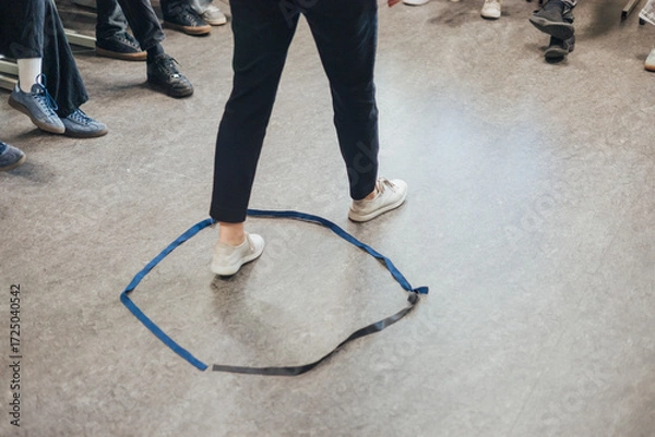 Fototapeta A student stands with feet apart inside a taped circle on the classroom floor, participating in a group activity focused on teamwork, practice, and interaction
