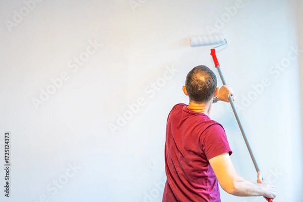 Fototapeta Man painting the wall with an extended roller during home renovation to reach higher surfaces. Concept of efficient interior work, broad coverage and advanced DIY improvement.