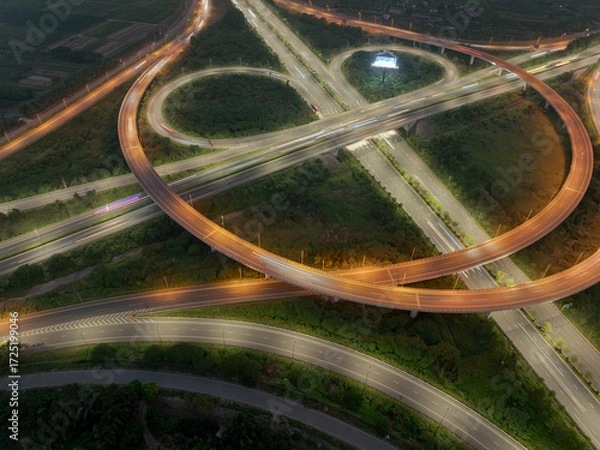 Fototapeta An aerial, high-angle shot of a glowing cloverleaf interchange in Hanoi at dusk, capturing the intricate curves and overpasses of the road network with subtle vehicle light trails.