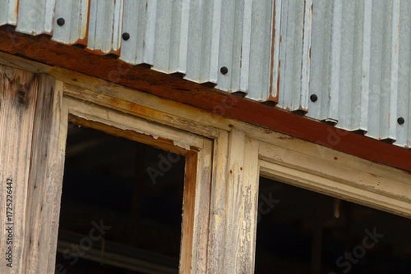 Fototapeta This is a charming wooden building characterized by its aged appearance, featuring a rusty metal roof alongside a thoughtfully placed window