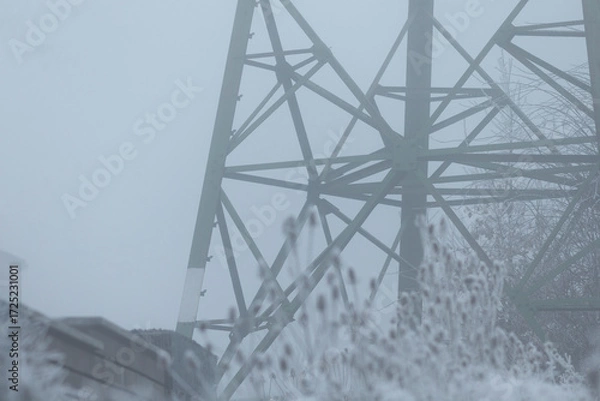 Fototapeta This is a black and white photograph depicting a power line that is situated in a thick layer of fog, creating a striking visual atmosphere