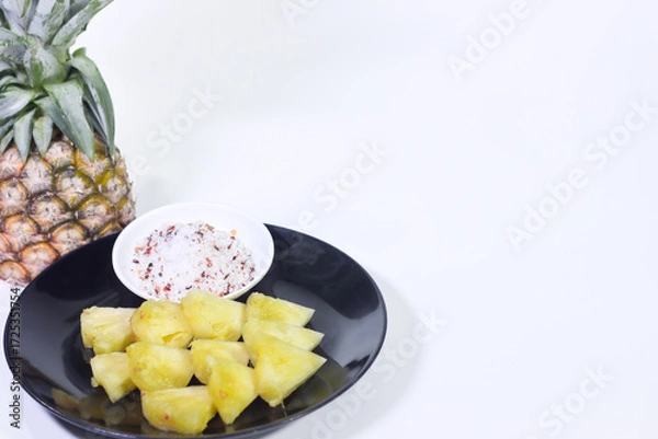 Fototapeta Close-up of Sliced Pineapple on a Black Plate with Dipping Sauce and a Whole Pineapple, White Background