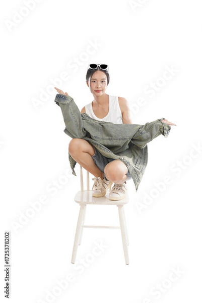 Obraz Stylish Pose on Chair: A young, attractive woman showcases contemporary fashion, posing confidently while seated, emphasizing modern trends, individuality, and the allure of high-style aesthetics.