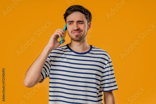 Fototapeta Disappointed young man looking at smartphone with hopeless expression on yellow