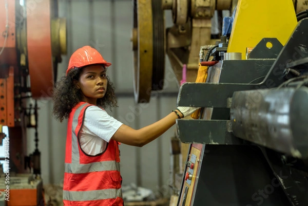Fototapeta A female worker in a steel factory is operating machinery. A woman is focused working on a machine in a factory.