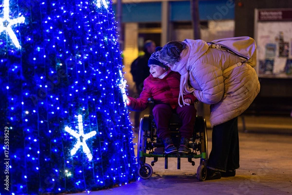 Fototapeta Happy child with disability admiring christmas tree lights with mother at night
