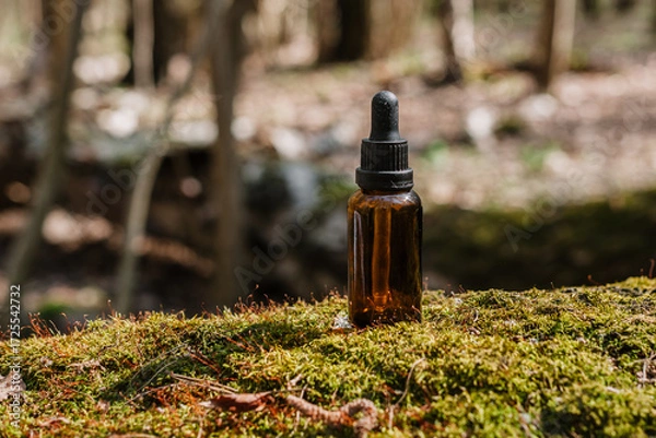 Fototapeta A dark and light glass serum bottle with a dropper, tree bark wood, moss. forest on a sunny day nature background. Concept of skin care, hydration, cosmetic demonstration eco-friendly product mock up