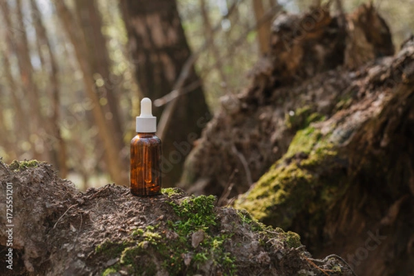 Fototapeta A dark and light glass serum bottle with a dropper, tree bark wood, moss. forest on a sunny day nature background. Concept of skin care, hydration, cosmetic demonstration eco-friendly product mock up
