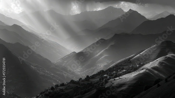 Fototapeta Sunlight piercing through clouds onto layered mountain ranges in a dramatic black and white landscape.