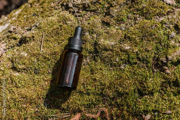 Fototapeta A dark and light glass serum bottle with a dropper, tree bark wood, moss. forest on a sunny day nature background. Concept of skin care, hydration, cosmetic demonstration eco-friendly product mock up