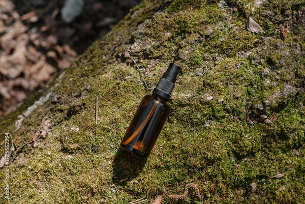 Fototapeta A dark and light glass serum bottle with a dropper, tree bark wood, moss. forest on a sunny day nature background. Concept of skin care, hydration, cosmetic demonstration eco-friendly product mock up