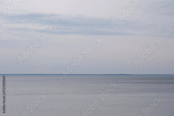 Fototapeta A tranquil lake under a cloudy sky with soft ripples and a distant horizon. Minimalist nature scene evoking calm, solitude, and introspection