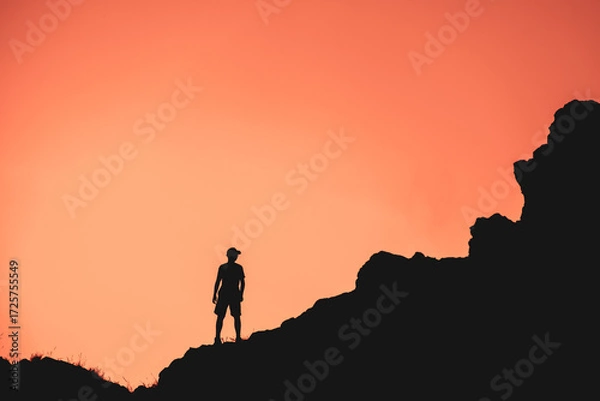 Fototapeta A man stands on a rocky hillside at sunset