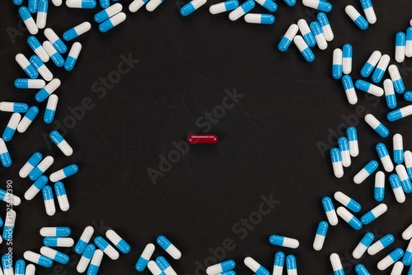 Fototapeta Red pill standing out from the crowd of blue capsules on a black background, a concept of choice, individuality, and unique thinking.