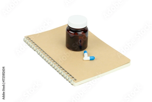 Fototapeta Amber glass medicine bottle with blue and white capsule pills on a notebook, isolated on white background with clipping path.
