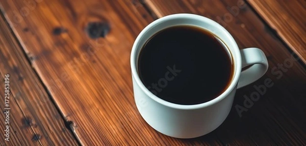 Fototapeta Close-up of a stark white mug filled with dark, rich coffee resting on warm, rustic wood,  minimalism,  texture