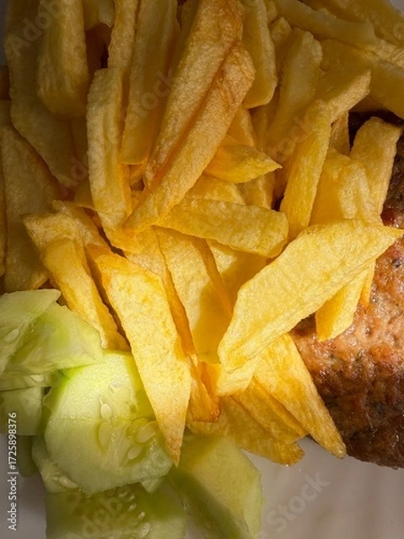Fototapeta Prepared food: fried potatoes, sliced ​​fresh cucumber, steak. Close-up of a prepared portion of food on a white plate.