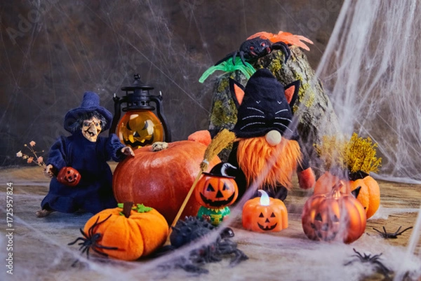 Fototapeta halloween, a cheerful witch with flowers and a gnome in a black cat costume stand near a big pumpkin at a noisy cobweb party with pumpkins and spiders, All Saints Day, horizontal, creative focus
