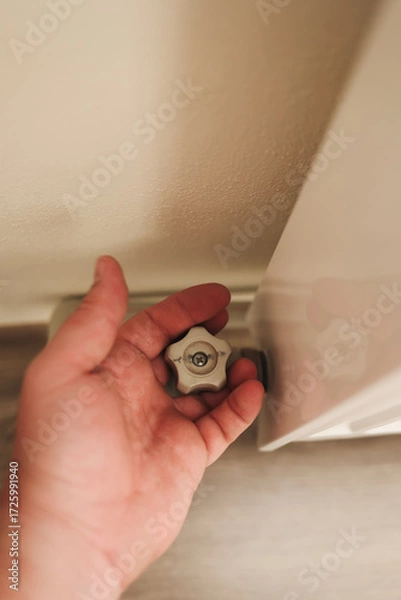 Fototapeta 
A close-up hand holding the radiator valve knob, symbolizing control of heating and energy use. The focus is on regulation, energy saving, and household heating balance.