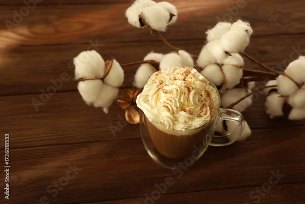 Fototapeta Warm coffee topped with whipped cream and spices beside soft cotton on a wooden table