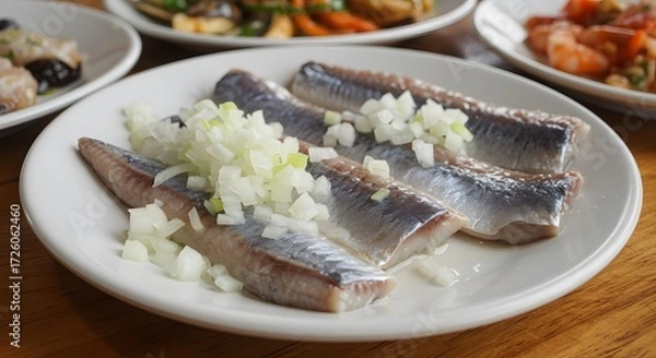 Fototapeta Close up of herring fillets topped with chopped onions on a white plate alongside other dishes