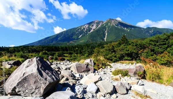 Fototapeta Volcanic peak backdrop behind rock strewn field, with forest belt and bright blue sky