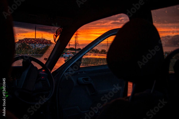 Fototapeta view from a car on the highway in bad weather conditions, rain and fog, at a beautiful red sunset