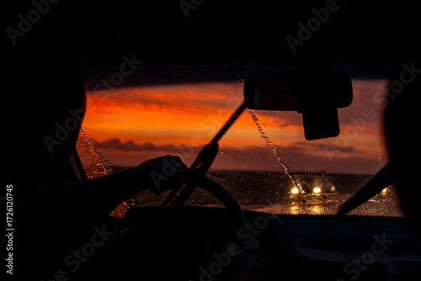 Fototapeta view from a car on the highway in bad weather conditions, rain and fog, at a beautiful red sunset