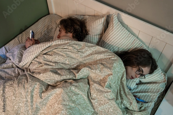 Fototapeta Couple lying in bed ignoring each other while using smartphones, illustrating digital addiction, relationship problems, emotional disconnection and modern lifestyle issues.