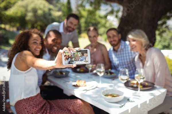 Fototapeta Friends taking selfie on mobile phone while having meal