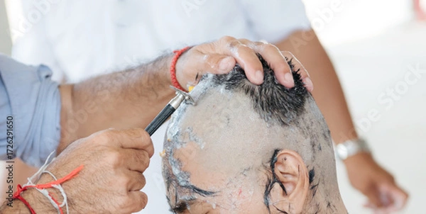 Fototapeta Close-up of a man having his head shaved clean with a straight razor, foam and hair remnants visible on scalp.
