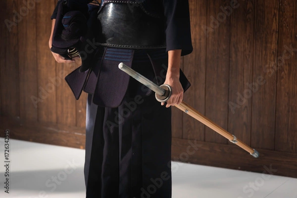 Fototapeta Portrait of man kendo fighter with bokuto Kendo gloves, helmet and bamboo sword on a wooden surface. Kendo armor.