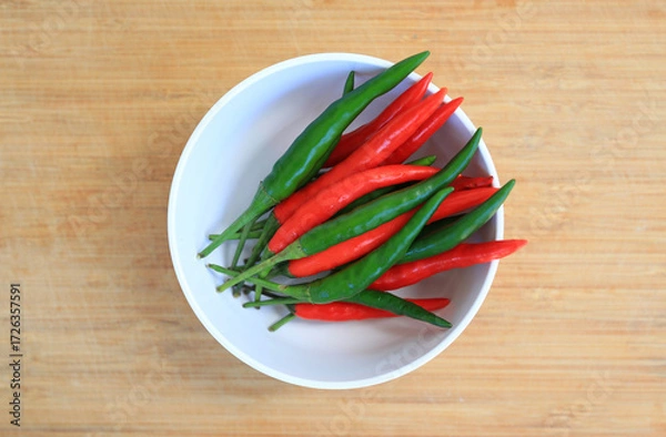 Fototapeta Red and green chili peppers in white bowl on bamboo wooden background, preparation process of chilli for cooking. Top view.