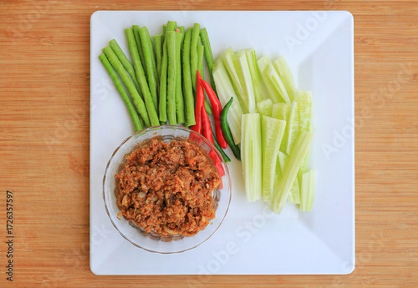 Fototapeta Stir fried pork with chili paste in bowl serve with vegetables on white plate against wooden background, Top view.