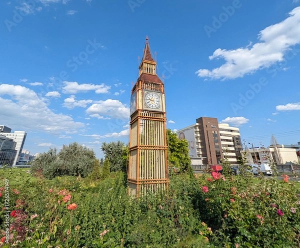 Fototapeta Big Ben tower as a scale model of a building of Houses of Parliament and Westminster pier. An imitation of the exterior of a famous building. A lightweight structure built on a flowerbed.