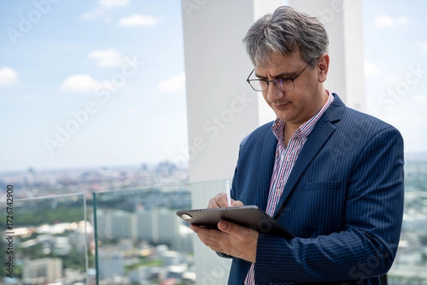 Fototapeta Mature businessman working with tablet computer at office rooftop with city background 