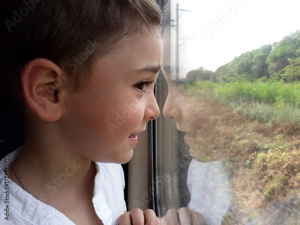 Fototapeta Young caucasian child enjoying train ride while looking out window