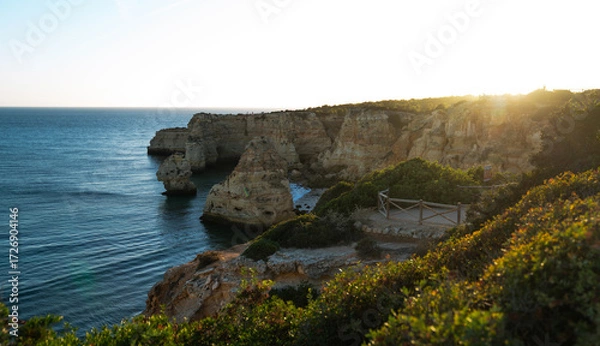Fototapeta the sun sets, its golden light bathes the rugged cliffs and serene waters of the coastline, highlighting the dramatic rock formations and the lush greenery atop this scenic Mediterranean landscape
