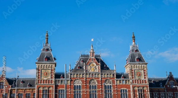 Fototapeta Central Station in Amsterdam, Netherlands, showcasing its neo-Renaissance architectural style with intricate details, spires, and decorative elements under a clear blue sky.