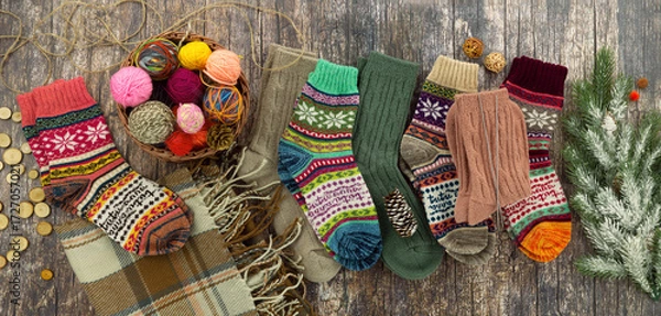 Fototapeta Colorful, warm knitted socks for cozy winter. Knitted socks, yarn, and a spruce branch on a wooden background. Panoramic image.