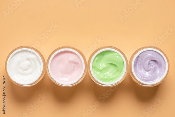 Fototapeta Various colored cosmetic creams in open jars on pastel yellow background in a row, top view, flat lay,