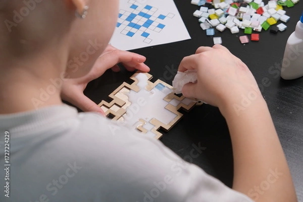 Obraz A girl makes a Christmas toy with her own hands from ceramic mosaic. Ceramic mosaic, DIY Christmas tree toy. Eco-friendly toy, educational activity for children.