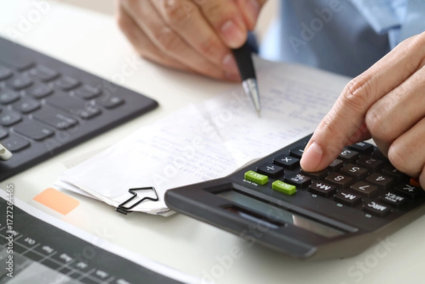 Fototapeta Businessman calculating expenses with calculator and financial documents