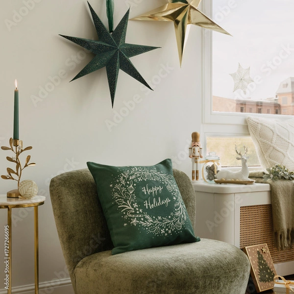 Fototapeta Green velvet chair with “Happy Holidays” cushion under paper stars, candle, nutcracker and reindeer on the windowsill create a warm, modern Christmas corner.