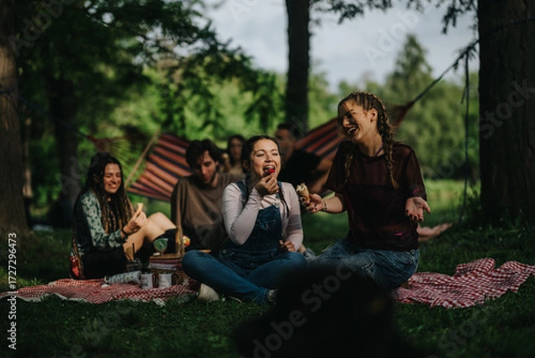 Fototapeta A cheerful group of friends having a picnic with food and laughter, relaxing outdoors.