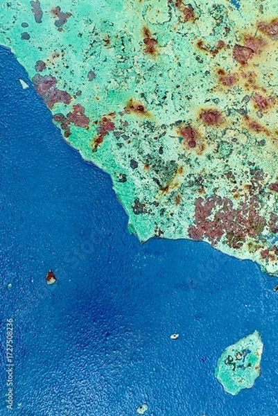 Fototapeta Close-up of old peeling green paint with patches of blue and rust on corroded metal surface, perfect for backgrounds and grunge design.