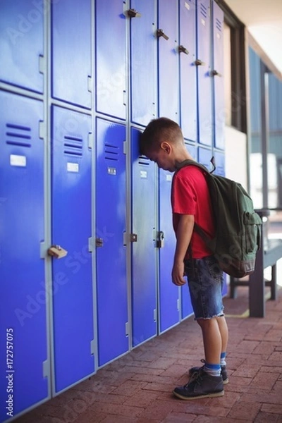 Fototapeta Side view of boy leaning on lockers in corridor